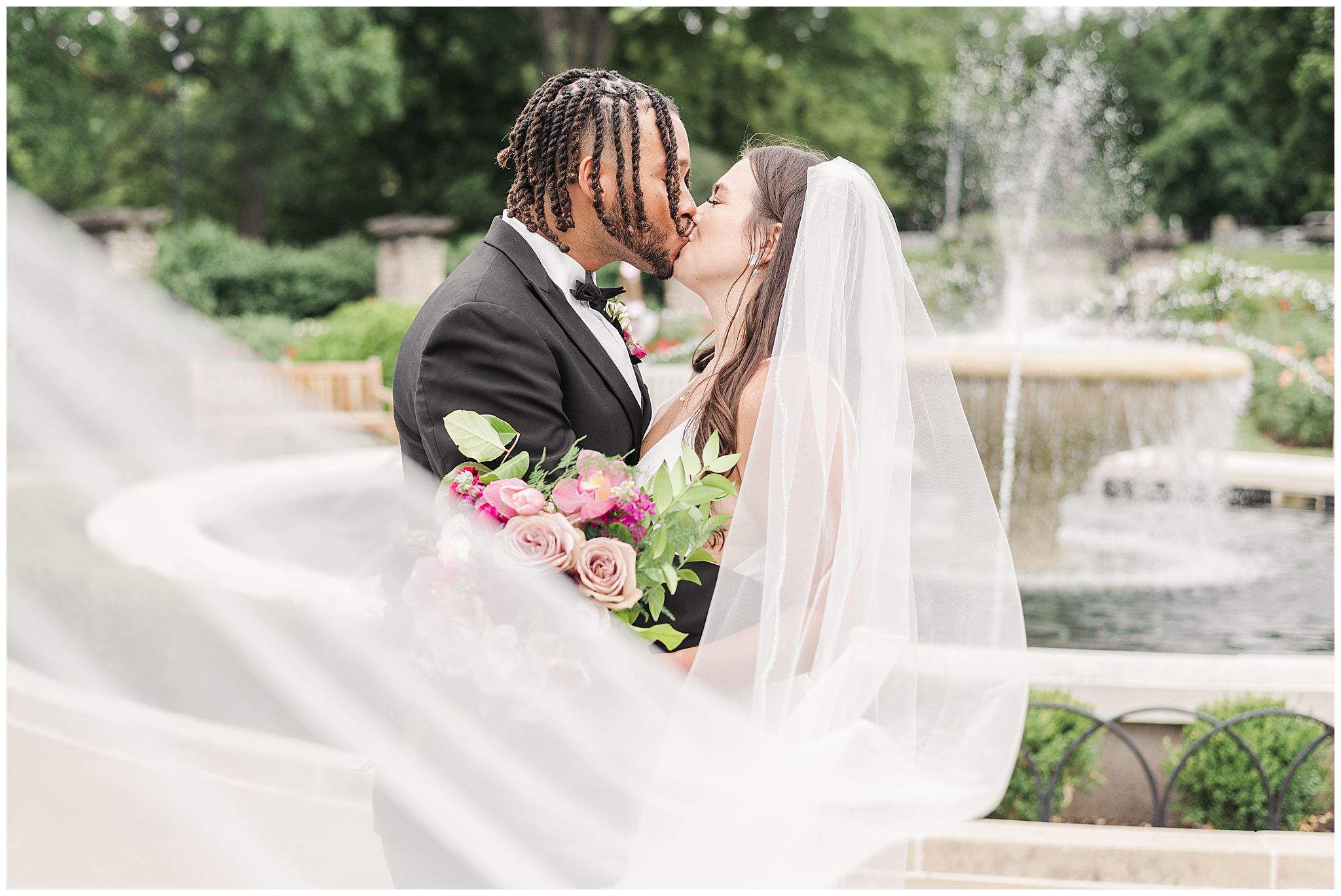 A bride and groom kissing as her veil sweeps in front of them at Loose Park in the Rose Garden in Kansas City.