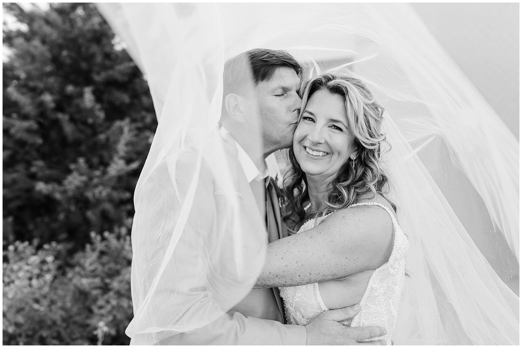 Black and white portrait of a bride and groom snuggled together under the brides veil on their wedding day in Kansas.