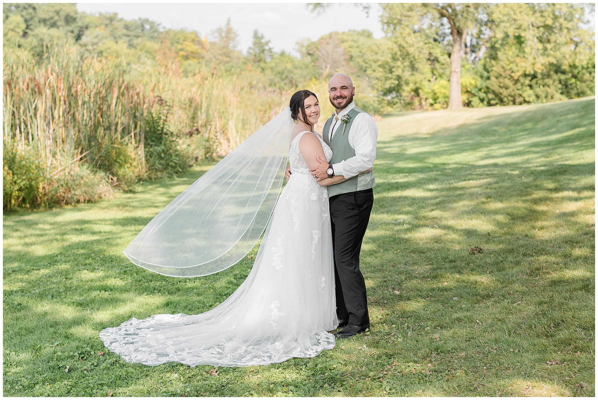 A classic portrait of a bride and groom smile on their wedding day as the brides veil flows behind her, taken by a Wisconsin wedding photographer!